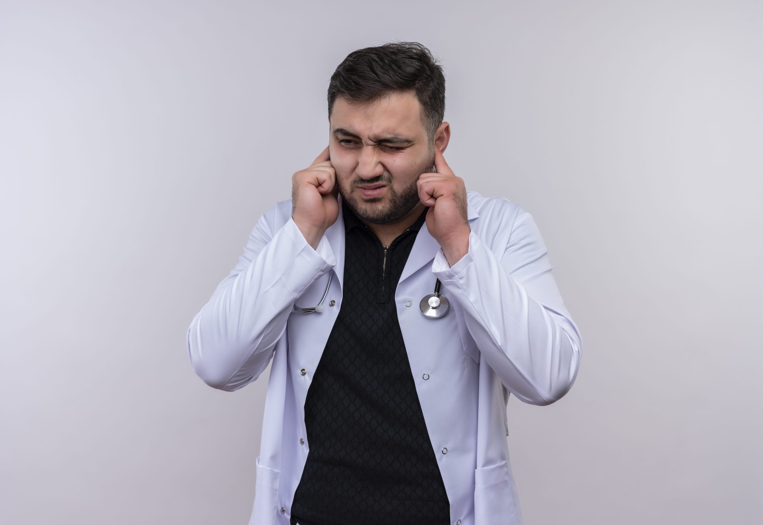 مجله وودمارت 25 young bearded male doctor wearing white coat with stethoscope closing ears with fingers with annoyed expression noise loud sound scaled